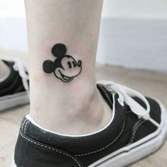 a small tattoo on the ankle of a person with mickey mouse head in black and white