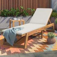 a wooden lounge chair sitting on top of a rug next to a potted plant