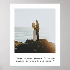 a man and woman standing on top of a rock next to the ocean holding each other