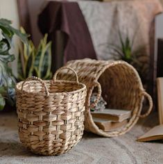 two woven baskets sitting on top of a floor next to books and plants in front of a bed