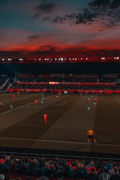 a group of people standing on top of a soccer field at night with the sun going down