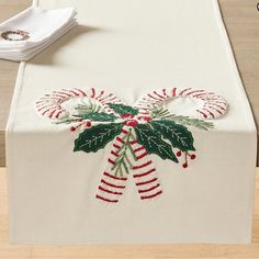 an embroidered table runner with holly and candy canes on it, sitting on top of a wooden table