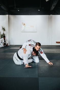 two men in black and white uniforms are doing karate moves on mats while one man is holding his leg up