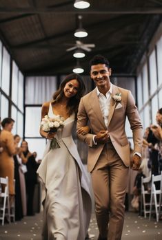 A bride and groom, hand in hand, walking down the aisle, their wedding attire radiating in dark beige and white. The scene captures the essence of pop inspo and the beauty of ready-made artistry, marking a moment of pure love and commitment. Beige And White Outfit Men, Groom Attire Tan, Old Money Groom Suit, Light Brown Groomsmen Suits, Beige Suit Wedding, Groom Suit Bow Tie, Beige Groom Suit, Beige Wedding Suit