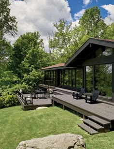 a large deck with chairs and tables in front of a house surrounded by wooded area