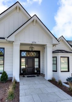 a white house with a black door and two plants on the front porch, along with stone walkway leading up to it