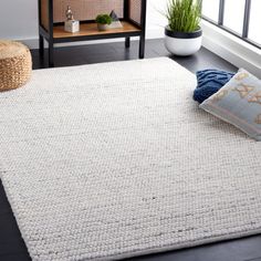 a white rug is on the floor in front of a window with plants and pillows