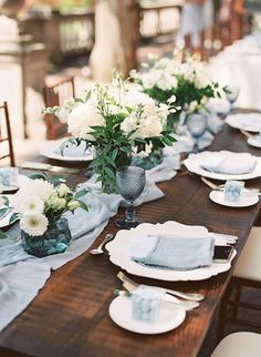 the table is set with white flowers and blue napkins