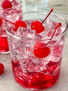 two glasses filled with ice and cherries on top of a table next to some water