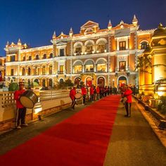 people are walking down the red carpeted walkway in front of a large building at night