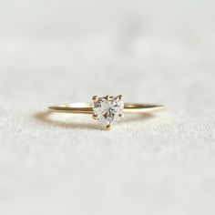 a gold ring with a heart shaped diamond on the front and side, sitting on a white surface