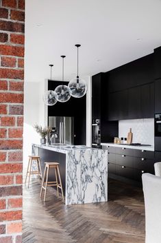 an open kitchen and dining room area with brick walls, marble counter tops and white chairs