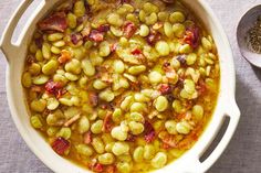 a pot filled with beans and bacon next to two spoons on top of a table