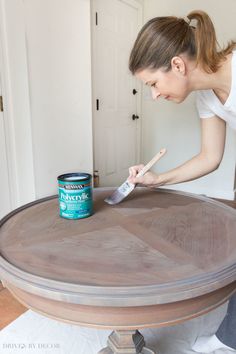 a woman painting a wooden table with a paintbrush