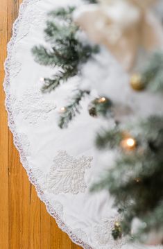 a white doily with pine branches and lights on the edge is sitting on a wood floor