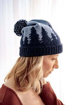 a woman wearing a knit hat with trees on the front and sides, looking off to the side