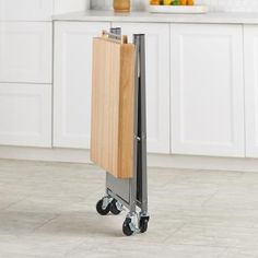 a wooden cutting board sitting on top of a metal rolling cart in a white kitchen