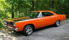 an orange muscle car parked in front of some trees