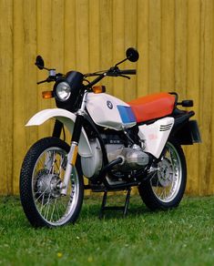 a white and red motorcycle parked in front of a yellow building with grass on the ground