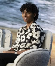 a woman sitting in a chair on the beach with headphones hanging from her ears