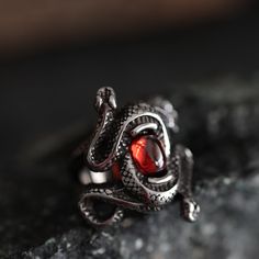 Enter the mystique with our Double Snake Ruby-Style Red Stone Gothic Ring--a mesmerizing fusion of gothic allure and intricate design. Crafted from durable stainless steel, this ring features two snakes coiled around a captivating ruby-style stone, creating a bewitching symbol of transformation and mystery.  Perfect for the woman who adores the enigmatic, this ring is not just an accessory but an extraordinary present that speaks volumes about her unique style and untamed spirit. -- Shipping inf Gothic Stainless Steel Metal Ring Jewelry, Black Fantasy Rings As Gift, Black Fantasy Style Rings As Gift, Fantasy Style Black Ring For Gift, Adjustable Gothic Snake Ring As Gift, Adjustable Gothic Snake Ring For Gift, Gothic Stainless Steel Ring As A Gift, Gothic Ruby Promise Ring, Gothic Garnet Jewelry For Gift