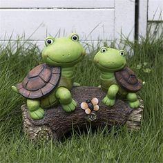 two little turtle figurines sitting on top of a log in the middle of some grass