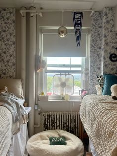 two beds in a bedroom with blue and white wallpaper, one has a round footstool