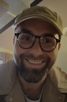 a smiling man wearing glasses and a hat