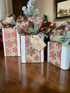 three small gift bags with bows on them sitting on a table next to a christmas tree