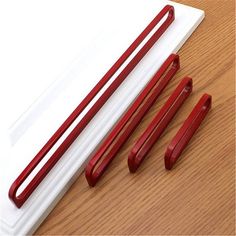 three red handled chopsticks on top of a wooden table next to a white cutting board