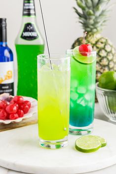 two glasses filled with different colored drinks on top of a white marble table next to a pineapple