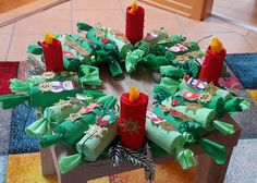 a wooden table topped with lots of green wrapped presents next to red candles and christmas decorations