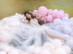 a woman laying on the ground surrounded by pink and white balloons, with her arms behind her head