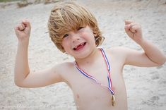 a young boy in a bathing suit with his hands up and smiling at the camera