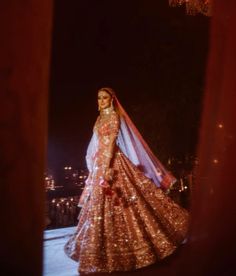 a woman in a pink and gold lehenga standing on a balcony at night