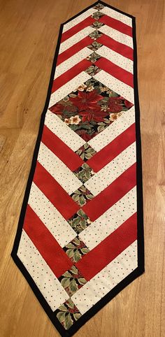 a red and white striped table runner with flowers on the border, sitting on a wooden floor