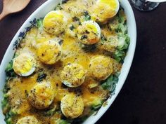 a dish with eggs and broccoli in it on a table next to a spoon