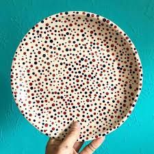 a hand holding a polka dot plate against a blue wall with black and red dots