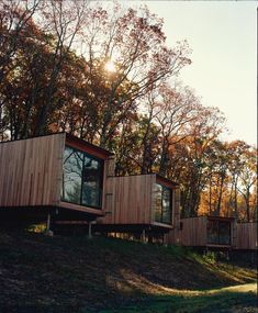 two wooden cabins sitting on top of a hill surrounded by trees and grass in the fall