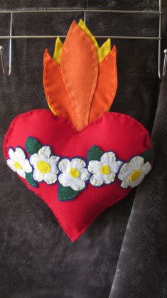 a red heart hanging on a clothes line with flowers and leaves attached to the hangers