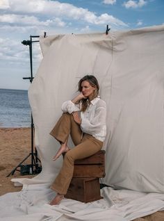 a woman sitting on top of a wooden stool in front of a white sheet covered backdrop