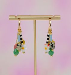 a pair of colorful earrings hanging from a gold earring stand on a pink background