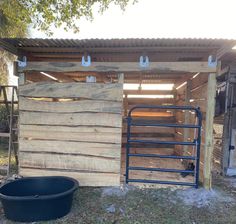 a wooden shed with metal bars on the side and a black bucket in front of it