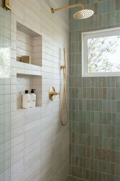 a bathroom with green tiled walls and white tile on the shower wall, along with shelves for toiletries