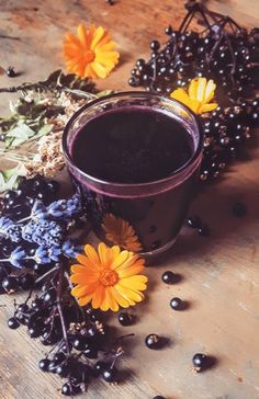 a cup filled with liquid next to flowers and berries