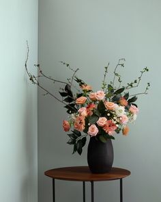 a black vase filled with pink and white flowers on top of a small round table