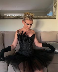 a woman sitting on top of a couch wearing black gloves and a dress with gold trim