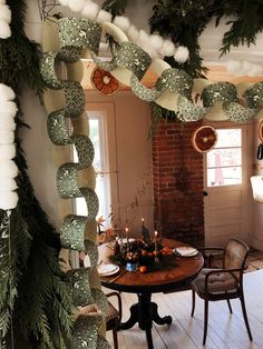 a dining room decorated for christmas with green and white decorations hanging from the ceiling, surrounded by greenery