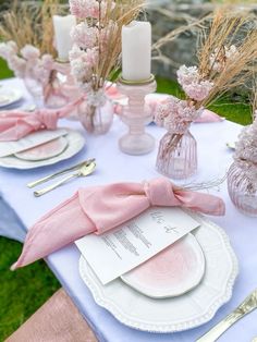 the table is set with pink napkins, plates and silverware in vases