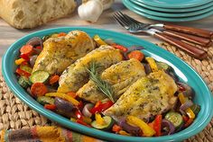 a plate with chicken and vegetables on it next to bread, utensils and napkins